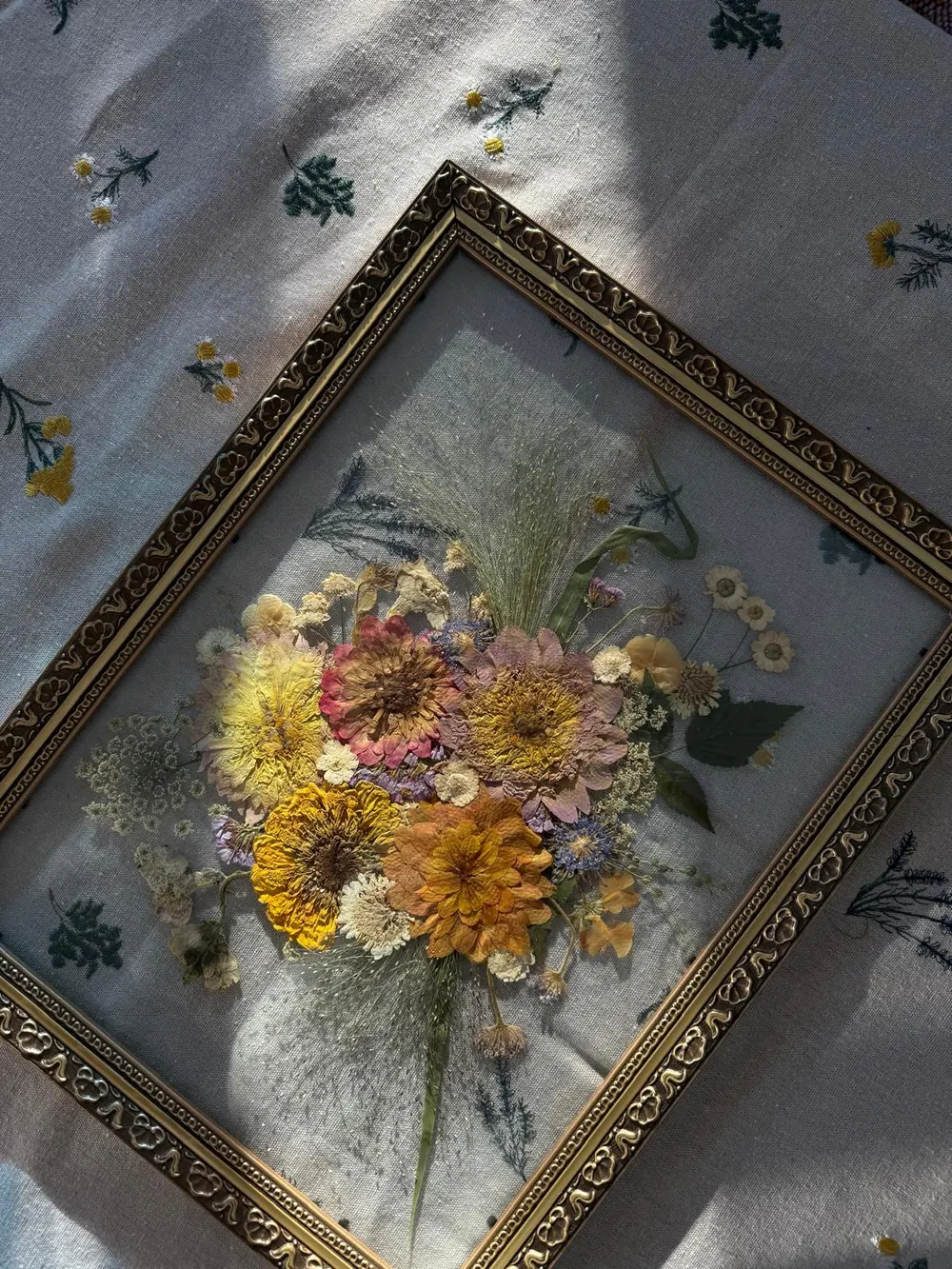 Ornate gold frame holding a warm-toned pressed bouquet of zinnias and grasses