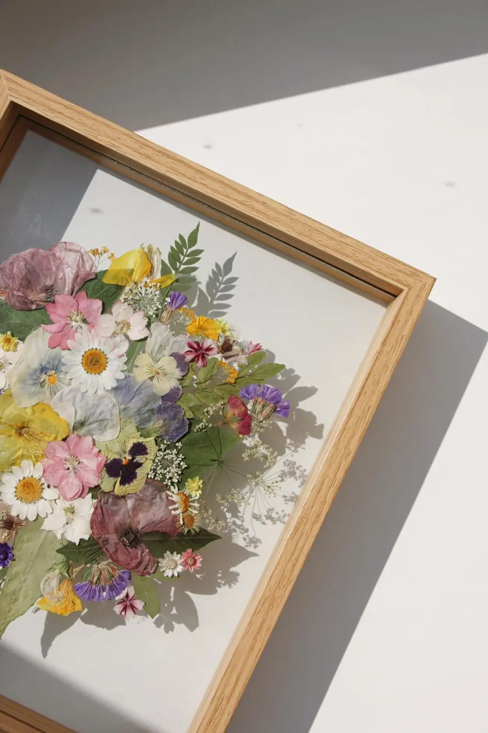 Pale oak frame with a full round pressed bouquet of daisies, pansies and roses